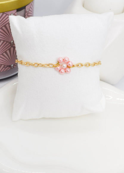 Gold bracelet with pink daisy flower made with pearls on a white cushion