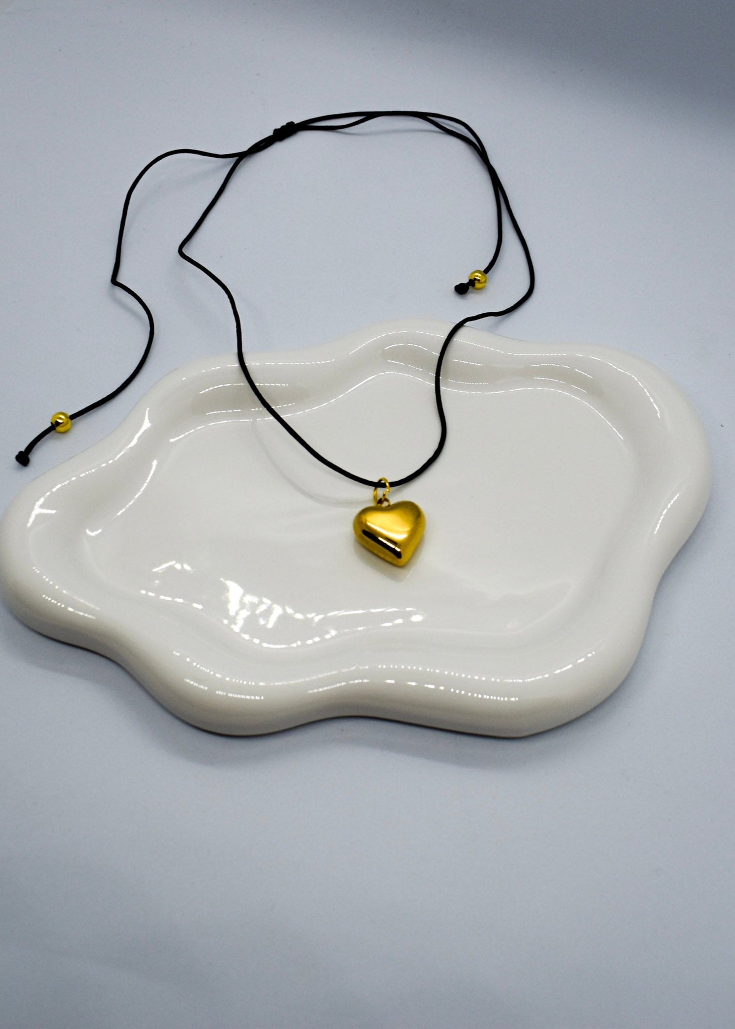 Gold heart pendant necklace on a white dish with a gray background