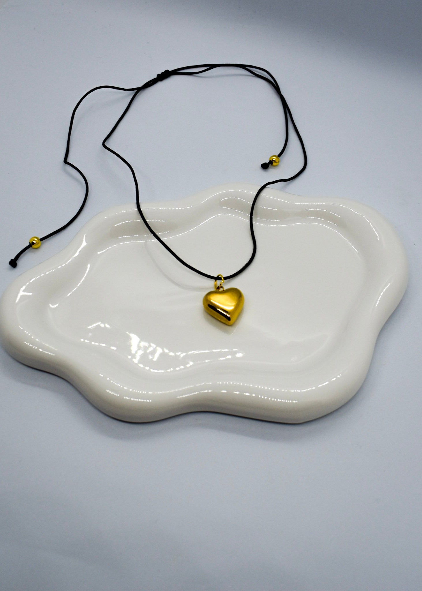 Gold heart pendant necklace on a white dish with a gray background