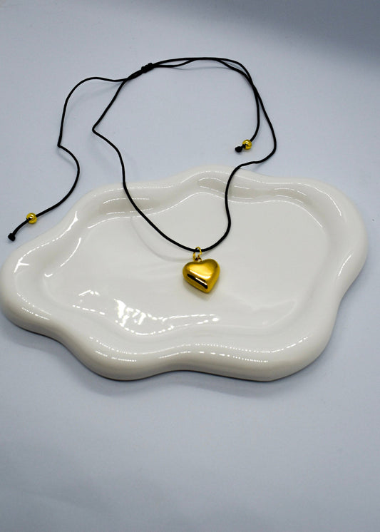 Gold heart pendant necklace on a white dish with a gray background