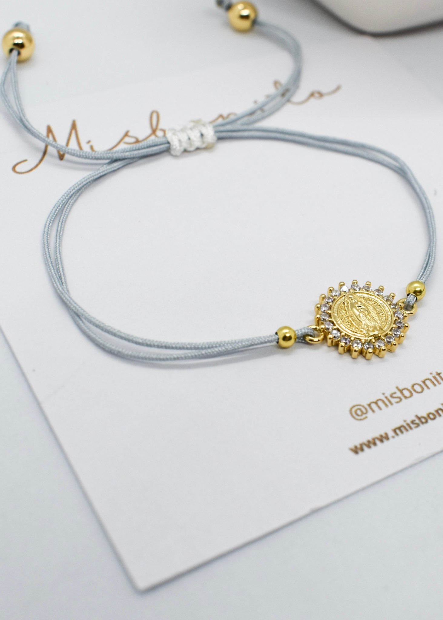 Gray bracelet with gold charm on a white card with 'misbonito' branding