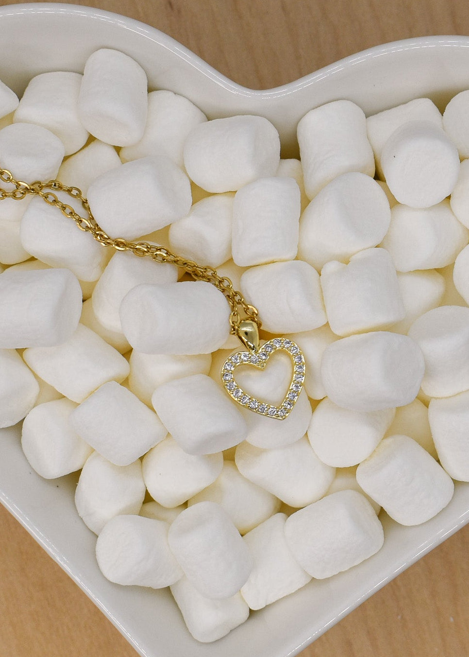 Heart-shaped dish filled with marshmallows and a gold necklace on a wooden surface