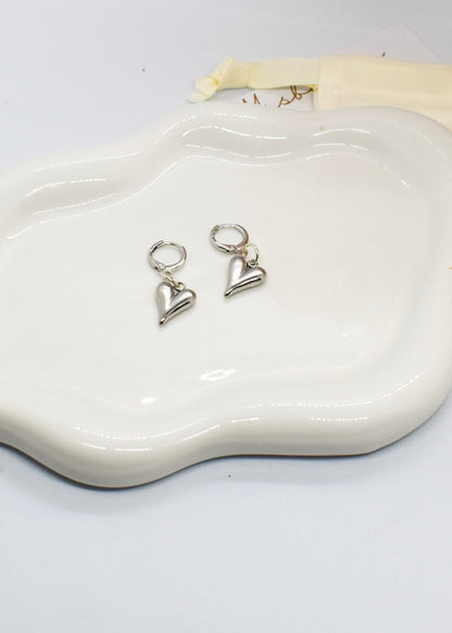 Heart-shaped silver earrings on a white dish with a white background