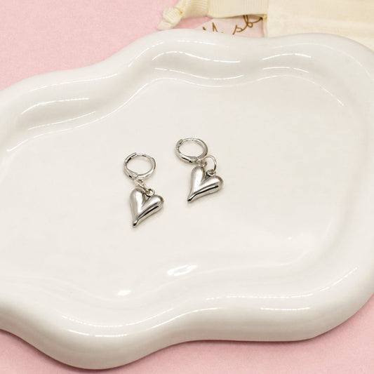 Heart-shaped silver earrings on a white dish with a white background