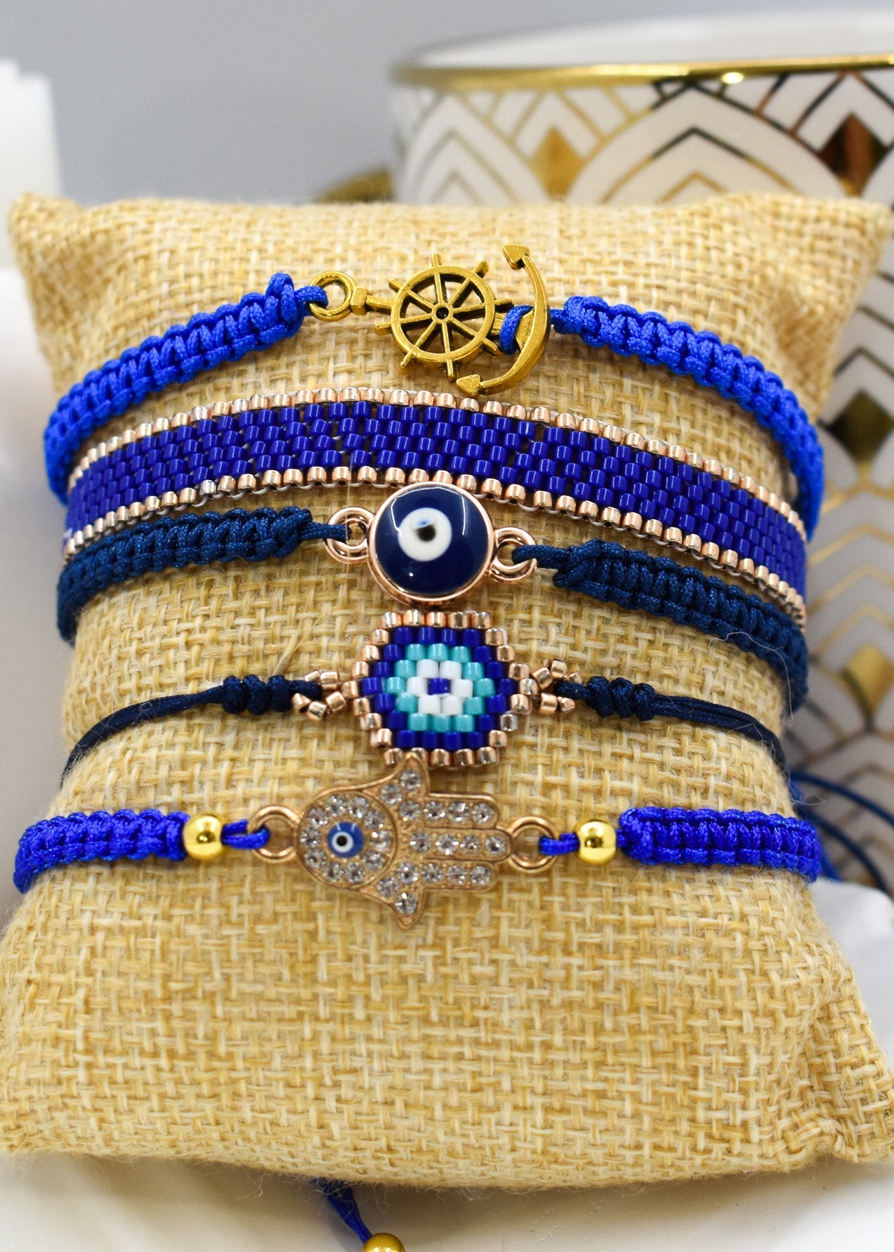 Set of blue and gold bracelets with evil eye and hamsa hand designs on a textured surface.