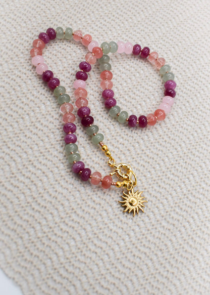 Multicolored beaded necklace with a gold charm on a textured beige background