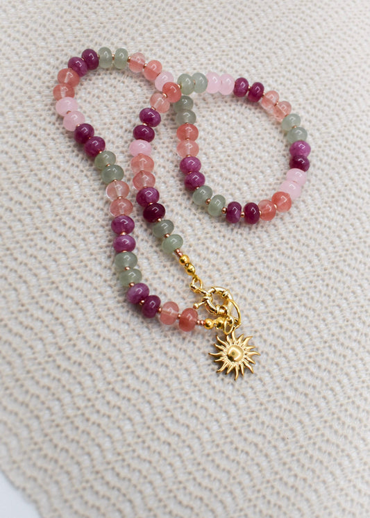 Multicolored beaded necklace with a gold charm on a textured beige background