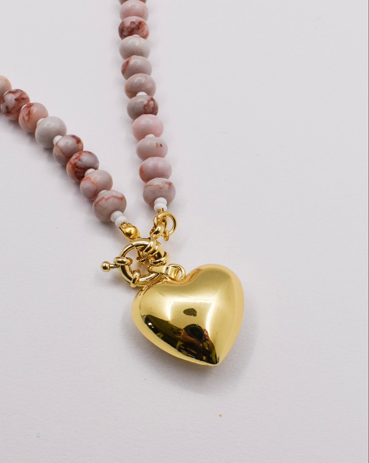 Necklace with pink beaded chain and gold heart pendant on a white background