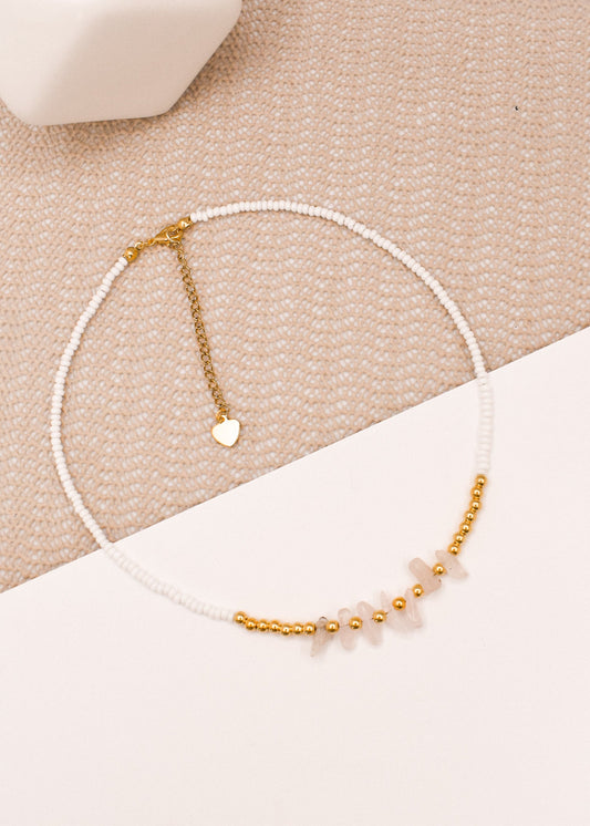 Necklace with white beads, rose quartz chips and gold accents on a beige surface