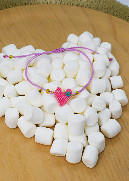 Pink bracelet with a heart charm on a bed of white marshmallows