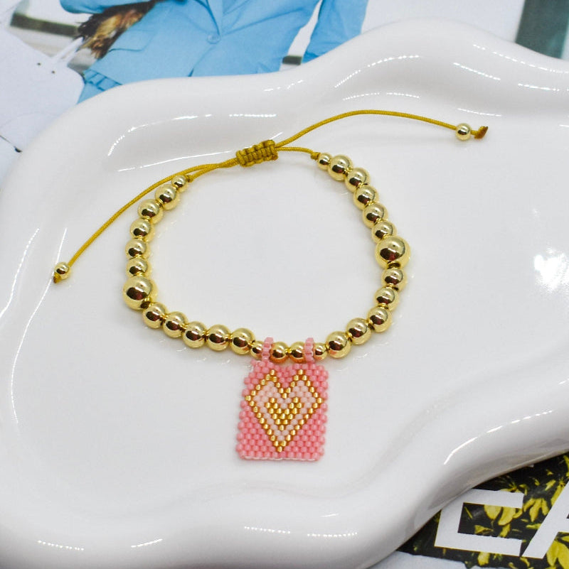 Bracelet with a pink heart charm on a white ceramic dish.