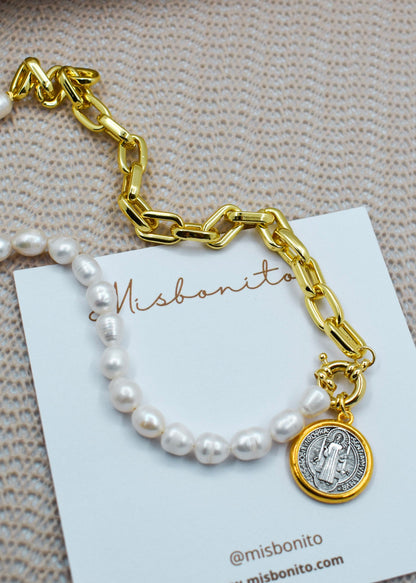 A gold chain bracelet with a white pearl strand and a Saint Benedict medallion charm, displayed on a white Misbonito brand card over a textured beige fabric background.
