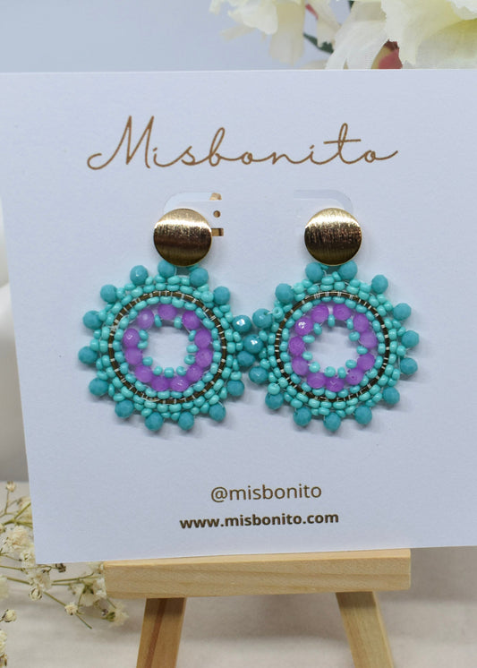 Turquoise and purple beaded earrings on a Misbonito branded card with a wooden stand.