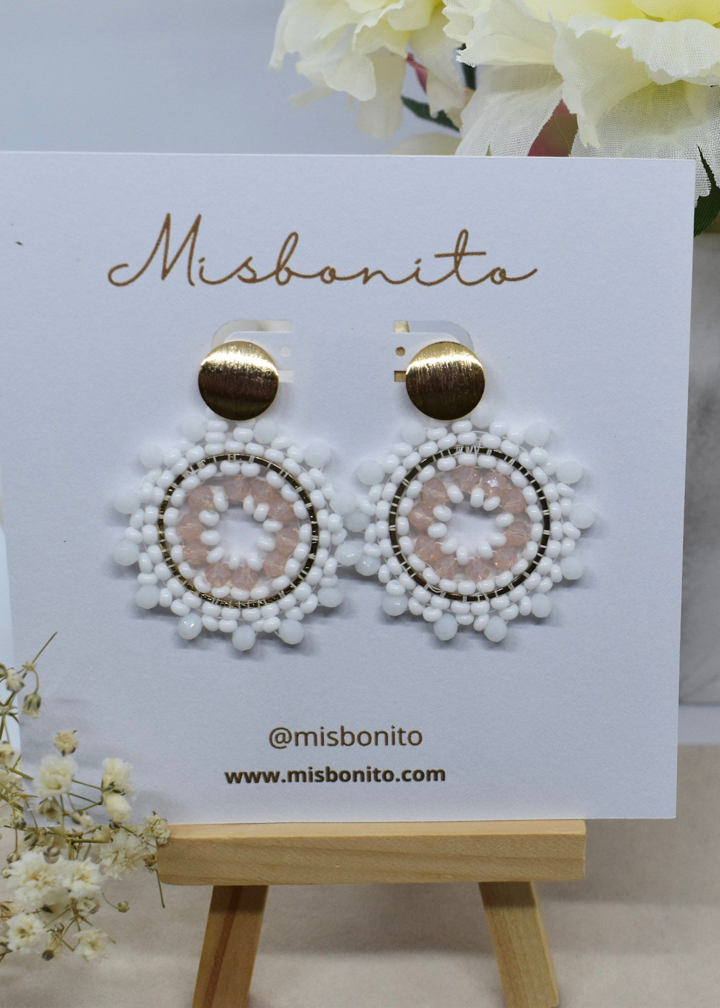 White beaded earrings on a Misbonito branded card with flowers in the background
