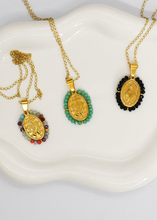 Three gold necklaces with pendants on a white dish