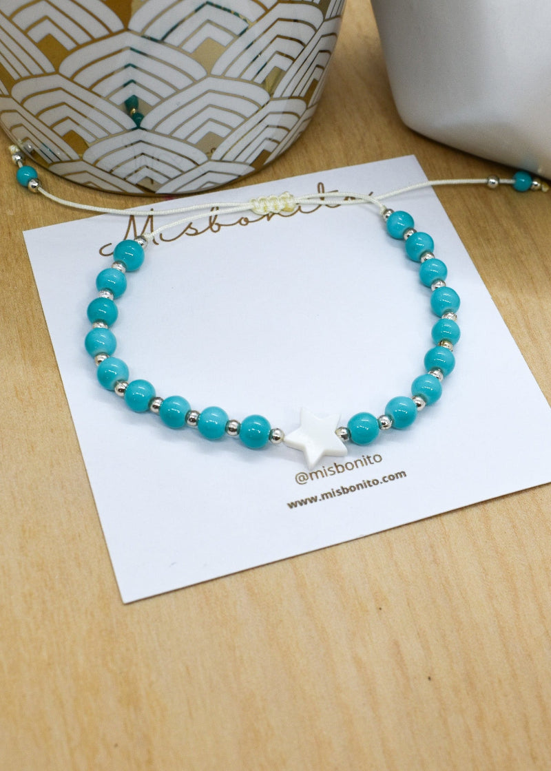 Turquoise beaded bracelet on a white card with 'Mishbonito' branding on a wooden surface.