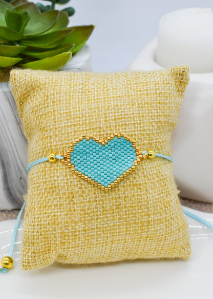 Turquoise heart-shaped bracelet on a yellow pillow with a plant in the background