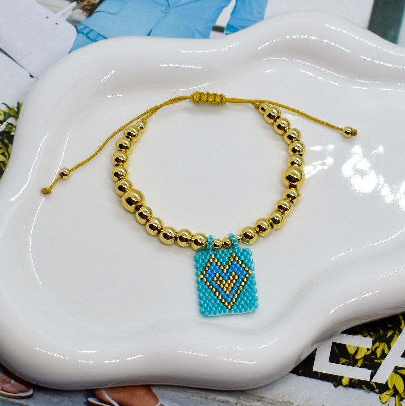 Gold beaded bracelet with a blue heart charm on a white dish.