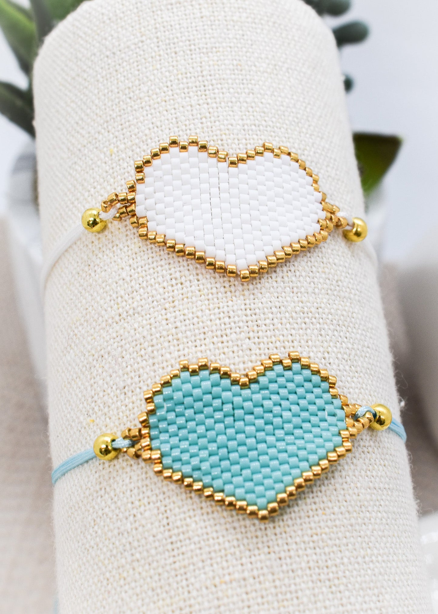 Two heart-shaped bracelets on a white cushion with a blurred green background