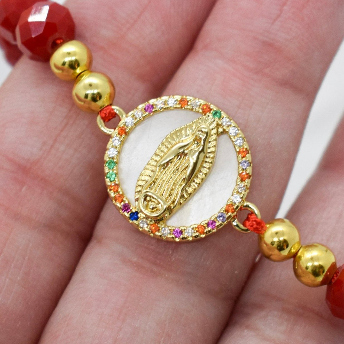 a hand holding a faceted crystal bracelet featuring a colorful zirconia virgin mary 