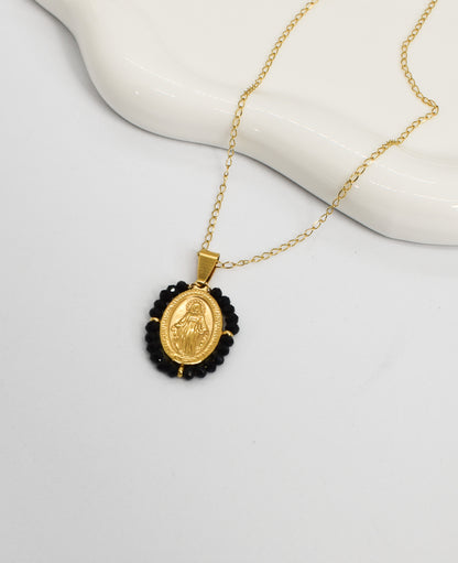 Gold necklace with a Virgin pendant surrounded by black crystals on a white background