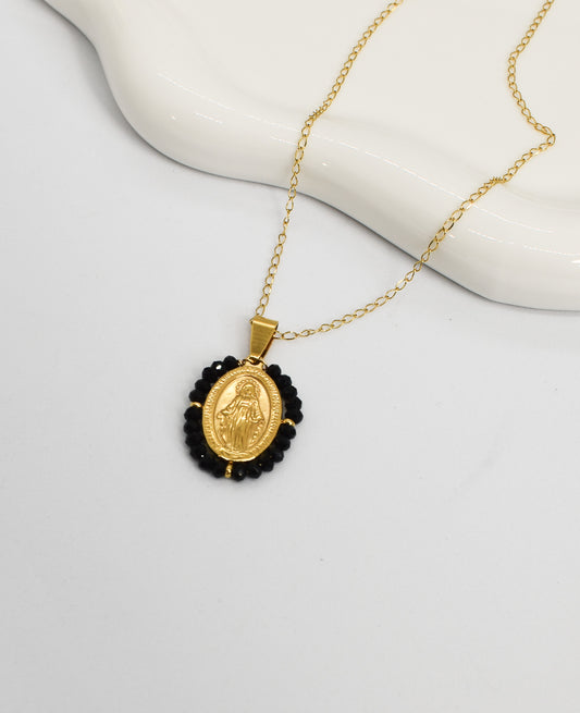 Gold necklace with a Virgin pendant surrounded by black crystals on a white background