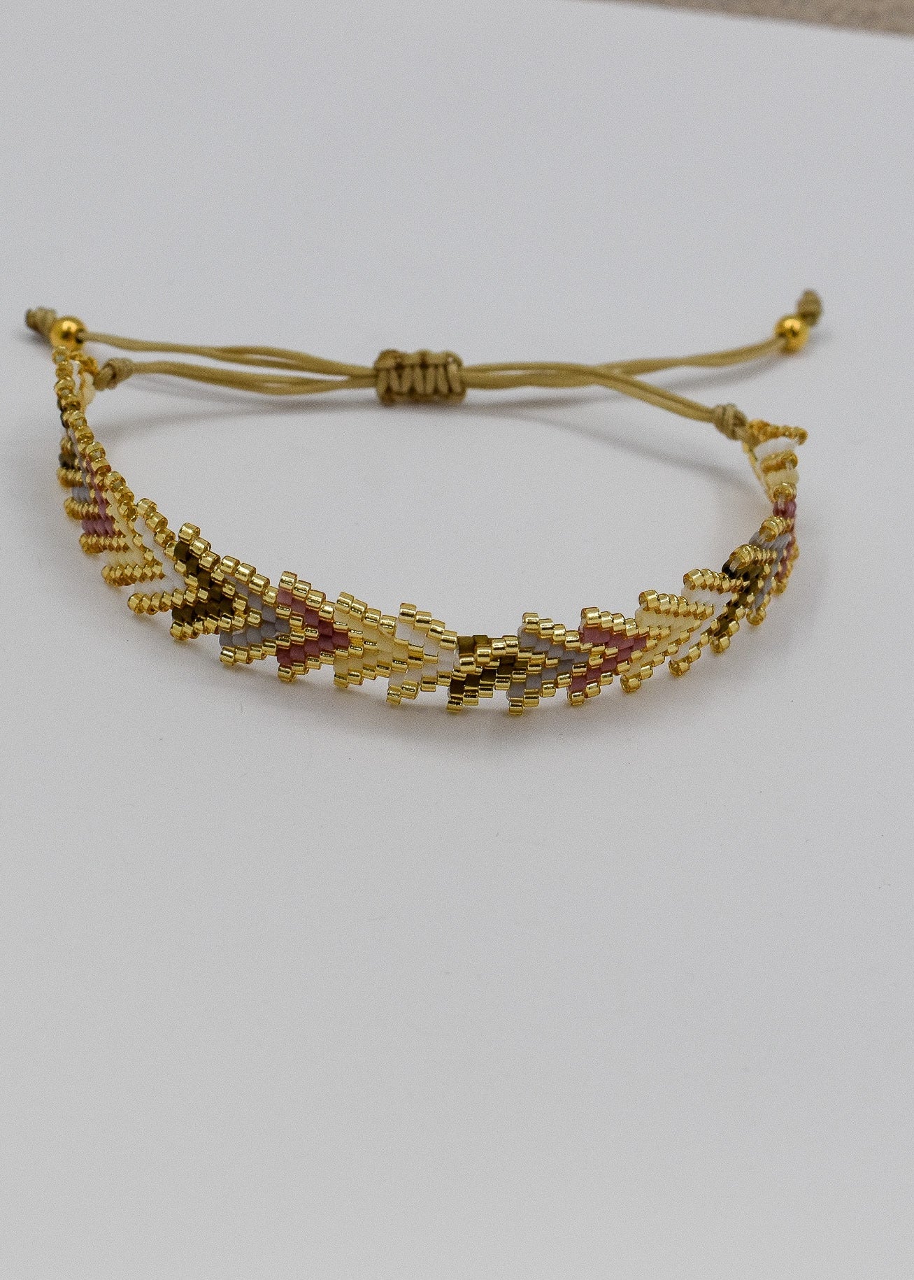 A gold beaded adjustable cord bracelet with a geometric chevron pattern, displayed on a plain white surface.