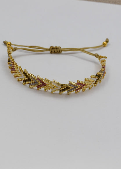 A gold beaded adjustable cord bracelet with a geometric chevron pattern, displayed on a plain white surface.