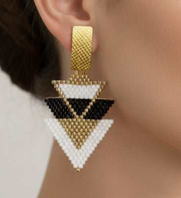 Pair of geometric triangle earrings with gold, black, and white design on a light gray background