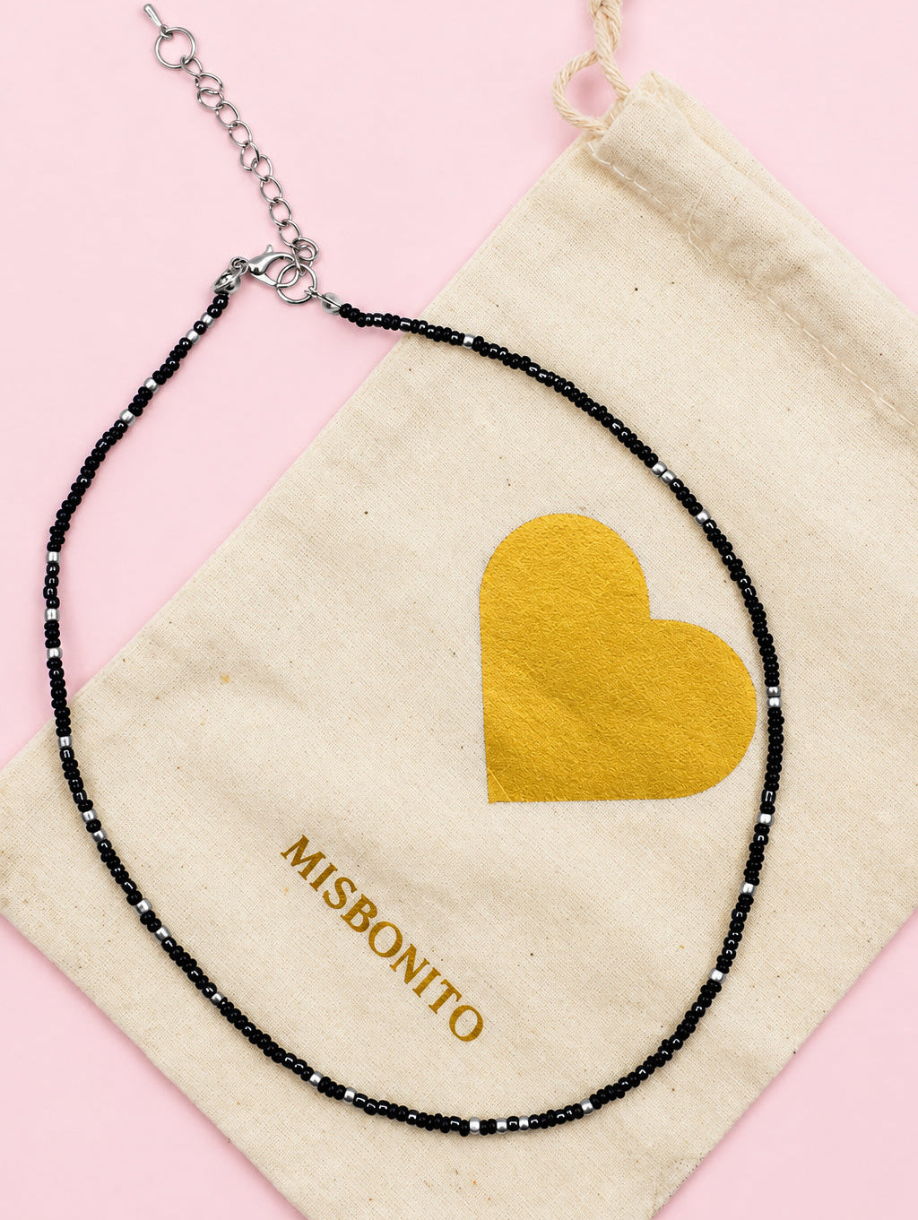 Necklace with black beads and gold heart pendant on a Misbonino pouch.