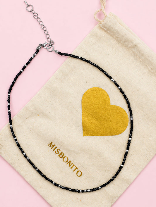 Necklace with black beads and gold heart pendant on a Misbonino pouch.