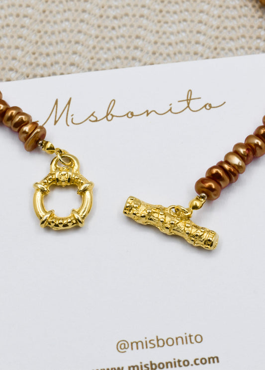 A close-up of a Misbonito beaded necklace with brown beads and gold-toned toggle charms, displayed on a white card with the Misbonito brand name.