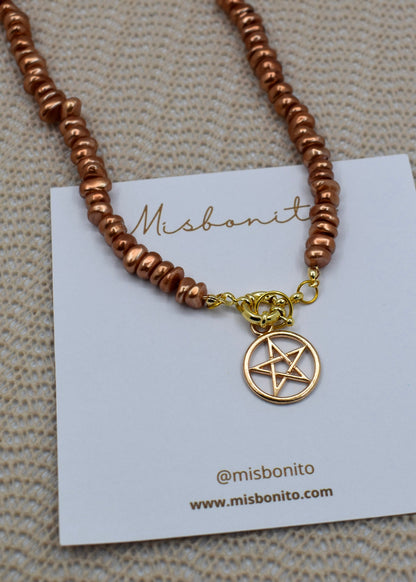 A copper-colored beaded necklace with a gold pentagram pendant, displayed on a white Misbonito brand card over a textured beige fabric background.