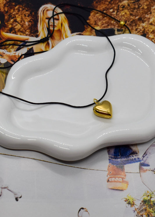 Gold heart-shaped pendant on a black cord with a white dish on top of a magazine
