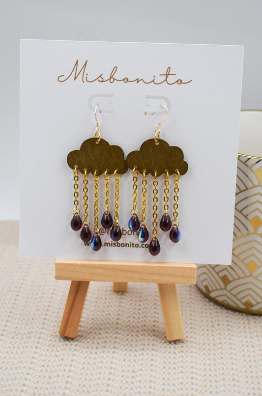 A pair of Misbonito dangling earrings displayed on a white card stand. The earrings feature dark brown cloud-shaped tops with gold-tone chains and teardrop beads hanging below.