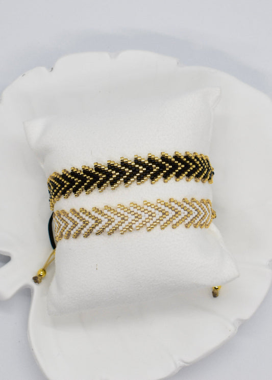 Gold and black beaded bracelet and white and gold beaded bracelet put on a pillow display
