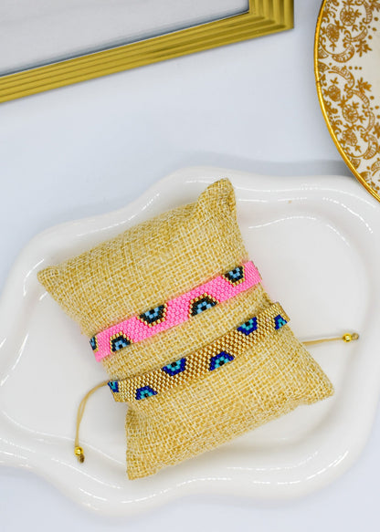 evil eye bar bracelet pink and gold on a pillow