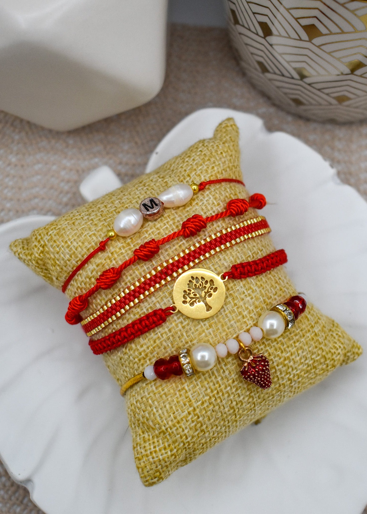 Set of bracelets with red strings and gold elements on a textured yellow pillow.