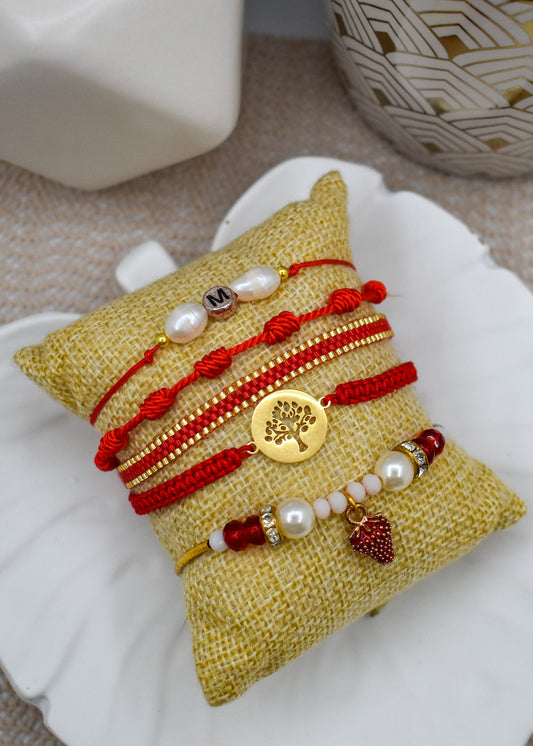 Set of bracelets with red strings and gold elements on a textured yellow pillow.