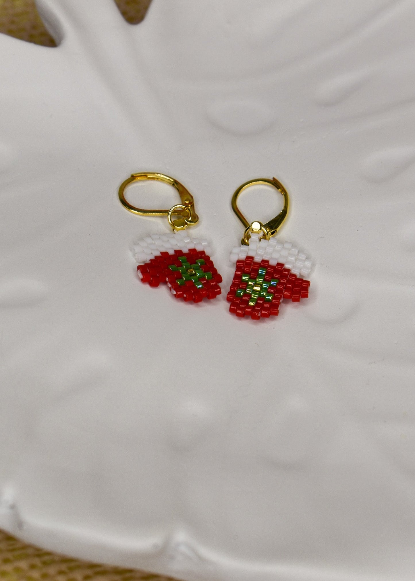 Gold earrings with red Christmas mitten designs on a white ceramic tray