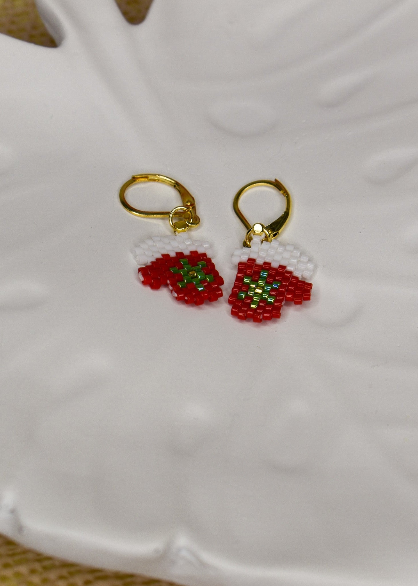 Gold earrings with red Christmas mitten designs on a white ceramic tray