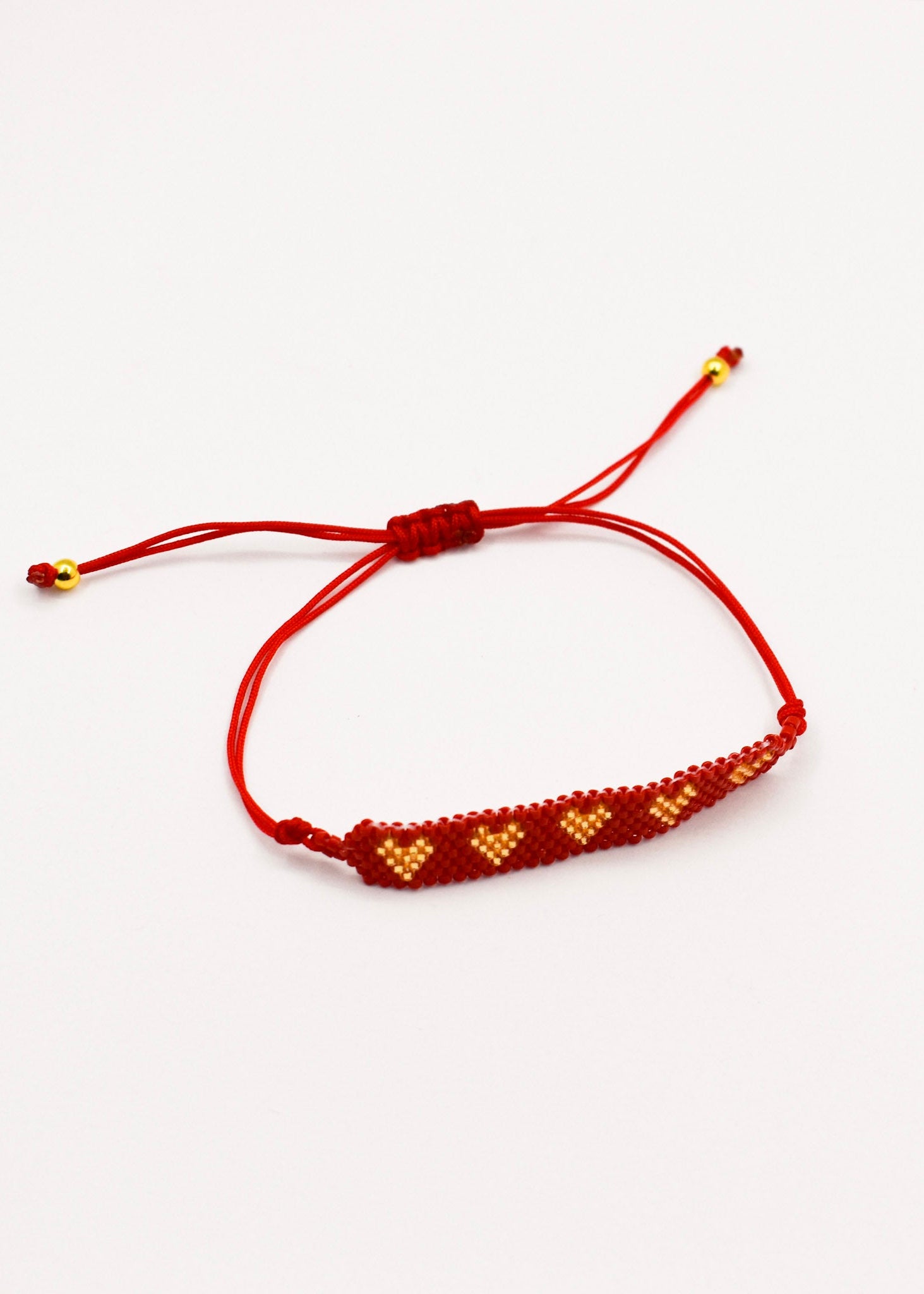 A red cord bracelet with a beaded bar featuring golden and red geometric patterns, shown on a plain white background.