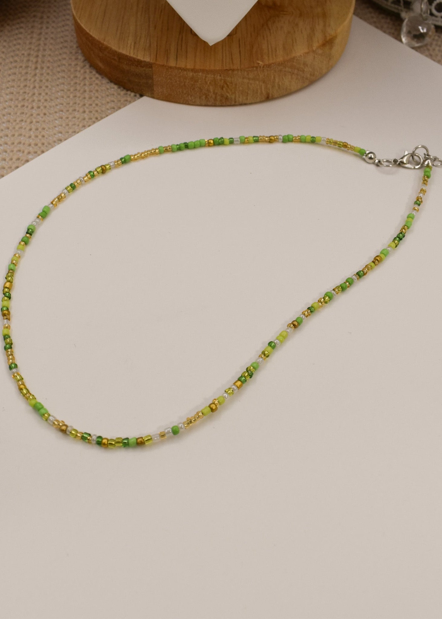 Green beaded necklace on a white surface with a wooden base in the background