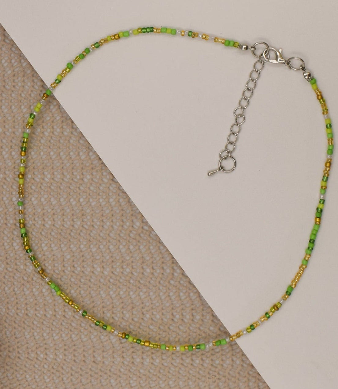 Green beaded necklace on a beige surface with a white object in the background