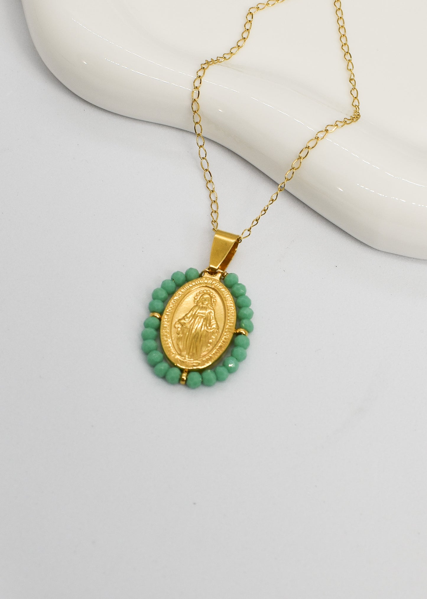 Gold necklace with a green beaded pendant on a white surface
