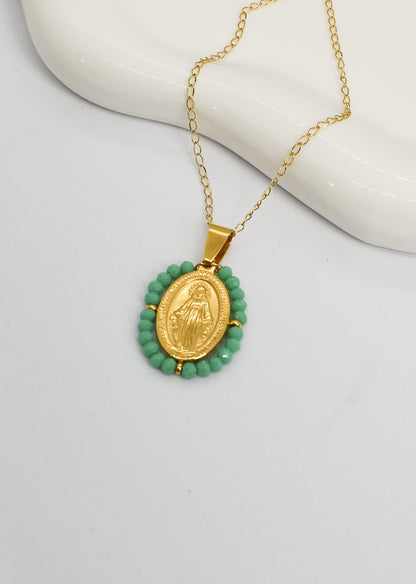 Gold necklace with a green beaded pendant on a white surface