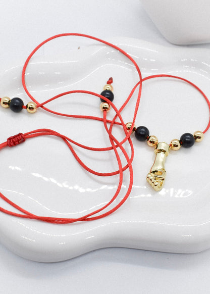 Red cord bracelet with black and gold beads and a hand charm on a white dish