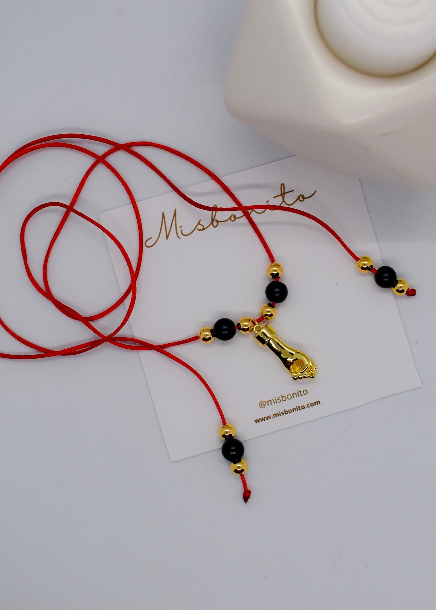 Red cord necklace with black and gold beads on a white card with 'Misbonito' branding.