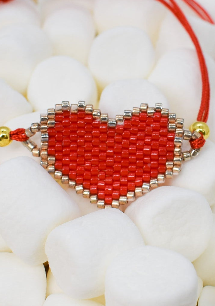 Red heart-shaped beaded charm on a red string with white stones in the background