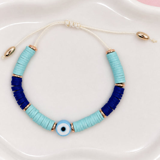 Bracelet with blue and gold beads on a white dish with flowers in the background